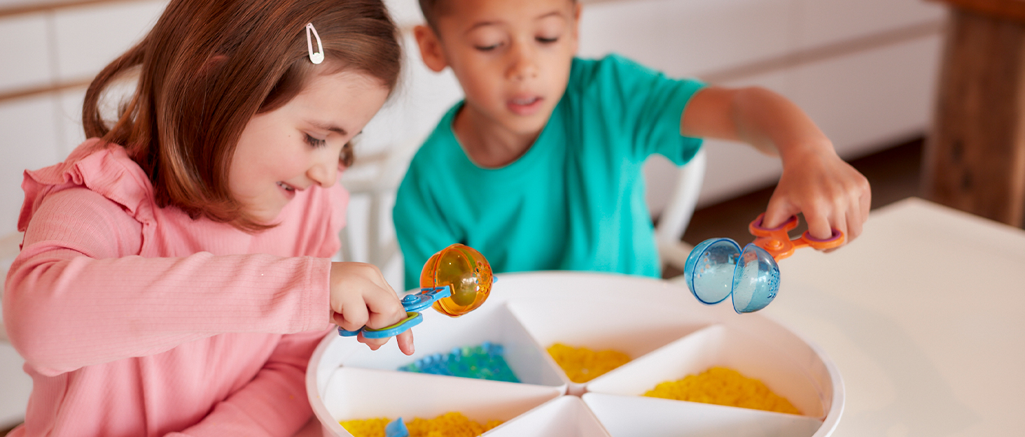 two children playing in a sensory tray with scoops